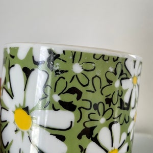 May include: A green ceramic mug with a white daisy pattern. The daisies have black outlines and yellow centers.