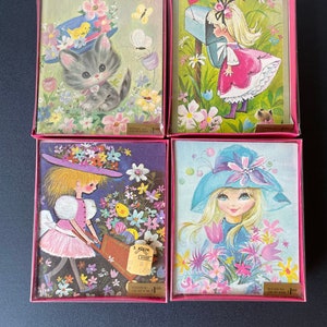 May include: Set of four vintage greeting cards featuring illustrations of girls and animals in a garden setting. The cards are in pink and white boxes with gold lettering. The cards are designed by S. Klein and have design numbers.