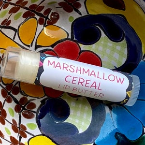 May include: A white tube of lip butter with a colorful label that says "Marshmallow Cereal Lip Butter".