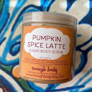 May include: A glass jar with a brown sugar body scrub labeled "Pumpkin Spice Latte Sugar Body Scrub" with the brand name "enough body" and the website www.enoughbody.etsy.com. The jar is 8 ounces or 227 grams.