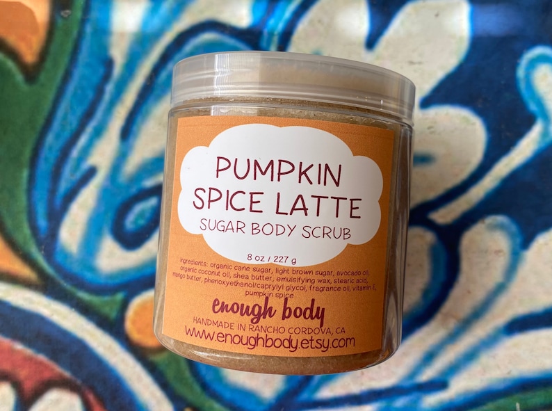 May include: A glass jar with a brown sugar body scrub labeled "Pumpkin Spice Latte Sugar Body Scrub" with the brand name "enough body" and the website www.enoughbody.etsy.com. The jar is 8 ounces or 227 grams.
