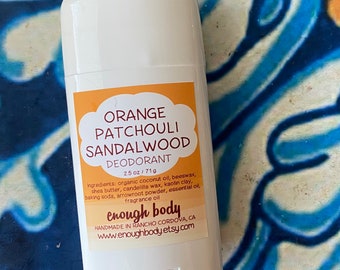 May include: A white deodorant stick with an orange label that reads "ORANGE PATCHOULI SANDALWOOD DEODORANT 2.5 oz / 71g" and lists the ingredients. The label also includes the brand name "enough body" and the website address "www.enoughbody.etsy.com".