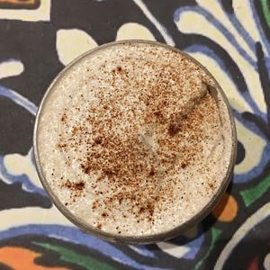 May include: A close-up of a white whipped cream topping with a sprinkle of brown cinnamon on top. The cream is in a clear glass container.