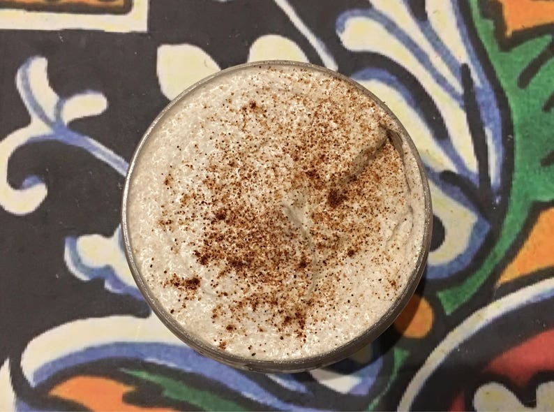 May include: A close-up of a white whipped cream topping with a sprinkle of brown cinnamon on top. The cream is in a clear glass container.