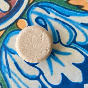 May include: A round, white, solid bar of soap on a blue and white patterned surface.