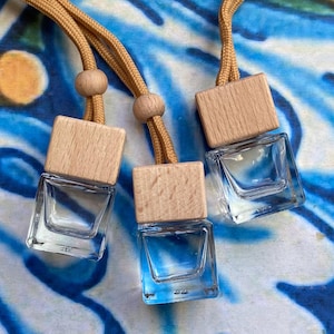 May include: Three clear glass bottles with wooden square caps and tan cords. The bottles are filled with a blue liquid. The background is a blue and white patterned surface.
