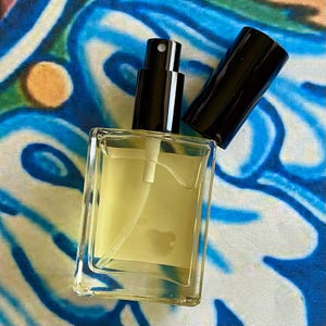 K&ouml;nnte beinhalten: Eine klare Glasflasche mit schwarzem Spr&uuml;hkopf und einer gelben Fl&uuml;ssigkeit im Inneren. Die Flasche steht auf einer blau-wei&szlig; gemusterten Oberfl&auml;che.