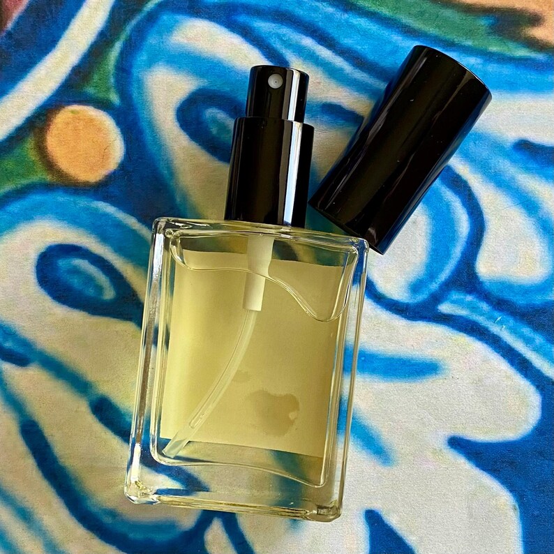 K&ouml;nnte beinhalten: Eine klare Glasflasche mit schwarzem Spr&uuml;hkopf und einer gelben Fl&uuml;ssigkeit im Inneren. Die Flasche steht auf einer blau-wei&szlig; gemusterten Oberfl&auml;che.