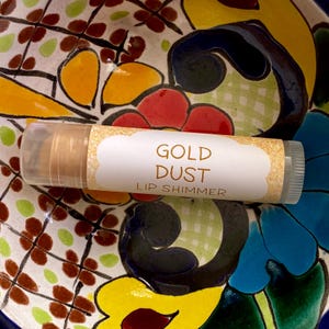 May include: A clear tube of gold lip shimmer with a white label that reads "GOLD DUST LIP SHIMMER".