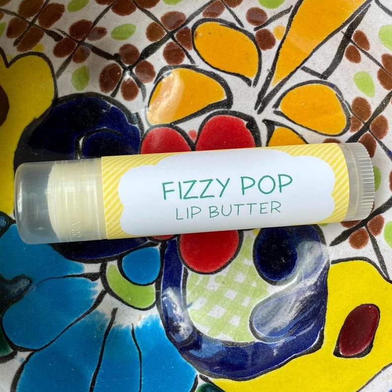 May include: A yellow and white striped lip balm tube with a white label that says "Fizzy Pop Lip Butter".