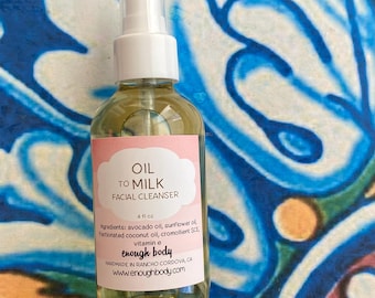 Puede incluir: Una botella de vidrio transparente con una bomba blanca y una etiqueta rosa. La etiqueta dice "OIL TO MILK FACIAL CLEANSER 4 fl oz Ingredients: avocado oil, sunflower oil, fractionated coconut oil, cromollient SCE, vitamin e enough body HANDMADE IN RANCHO CORDOVA CA www.enoughbody.com"