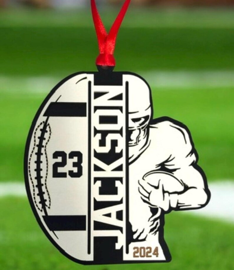 May include: A football-shaped ornament with a red ribbon. The ornament features a football player graphic and the name "JACKSON". The number "23" and the year "2024" are also displayed. Ideal for sports fans.
