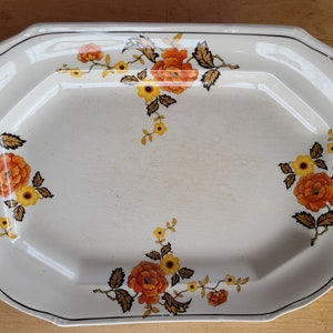 May include: A white octagonal serving platter with a floral design. The flowers are orange, yellow, and brown. The platter has a black rim.