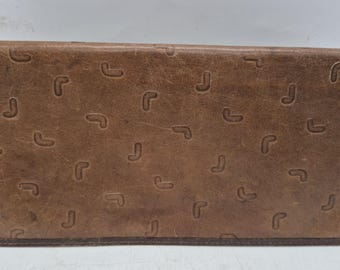 May include: A brown leather wallet with a repeating pattern of stylized "J" shapes. The wallet has a rectangular shape and a darker brown border. The leather appears worn, giving it a vintage look.