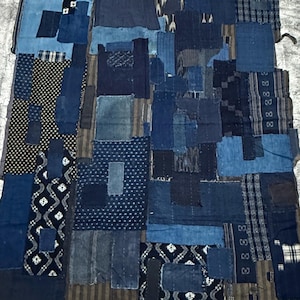 Può includere: Un tessuto rettangolare composto da numerosi ritagli di stoffa tinti in indaco in varie tonalità di blu, nero e marrone. Il patchwork presenta motivi diversi tra cui strisce, pois e forme geometriche, con un righello metallico da 91,4 cm.