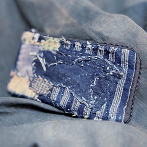 Könnte beinhalten: Eine rechteckige Reißverschlusstasche aus verschiedenen Blautönen, die ein Patchwork-Design mit sichtbaren weißen Nähten, ausgefransten Kanten und einer Kombination aus einfarbigen, gestreiften und strukturierten denimartigen Stoffen aufweist.