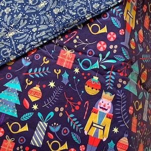 May include: Close-up of two sections of a Christmas-themed fabric. One section features a navy blue background with gold-colored nutcrackers, snowflakes, and other festive elements. The other section has a dark purple background with Christmas trees, ornaments, and gift boxes.