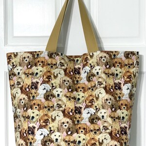 May include: A large canvas tote bag with brown straps. The bag is covered in a print of many different dog faces, all looking at the viewer. The dogs are mostly brown, white, and black.