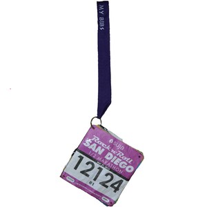 Puede incluir: Un dorsal de carrera rosa y blanco con el texto "Rock 'n' Roll San Diego 1/2 Marathon May 31, 2015" y el número "12124". El dorsal está sujeto a un cordón morado con el texto "My Bibs".