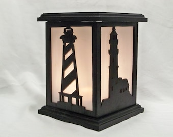 May include: Black wooden candle lantern with a frosted glass panel featuring two cut-out silhouettes of lighthouses. The lantern has a square base and a decorative top.