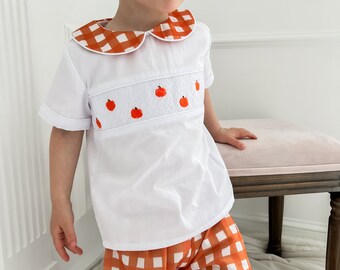 May include: A white short-sleeved shirt with an orange and white gingham collar and embroidered pumpkins. The shirt is paired with orange and white gingham shorts.