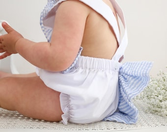 May include: A white baby romper with blue and white gingham print and a blue and white striped bow on the back.