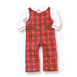 May include: A red plaid baby outfit with a white long-sleeved shirt. The outfit features a collared neckline and decorative buttons. The plaid pattern includes black and brown lines. The outfit is designed for infants and toddlers.