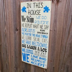 K&ouml;nnte beinhalten: Ein wei&szlig;es Holzschild mit blauem Text, auf dem steht: "In diesem Haus stimulieren wir, wir machen Routine, wir wiederholen, was wir sagen, wir machen eine sensorische Di&auml;t, wir lieben es, Dinge auszurichten, wir sehen uns die gleichen Dinge an, wir lernen soziale Hinweise, wir haben Ausraster, wir lachen viel, wir feiern alles, wir machen soziale Geschichten, wir lieben es, hart zu sein, Respekt, akzeptieren".