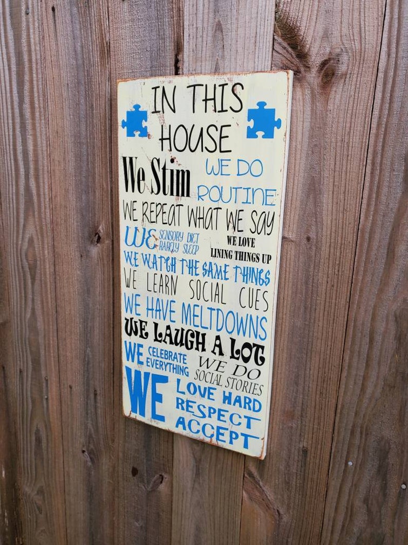 K&ouml;nnte beinhalten: Ein wei&szlig;es Holzschild mit blauem Text, auf dem steht: "In diesem Haus stimulieren wir, wir machen Routine, wir wiederholen, was wir sagen, wir machen eine sensorische Di&auml;t, wir lieben es, Dinge auszurichten, wir sehen uns die gleichen Dinge an, wir lernen soziale Hinweise, wir haben Ausraster, wir lachen viel, wir feiern alles, wir machen soziale Geschichten, wir lieben es, hart zu sein, Respekt, akzeptieren".