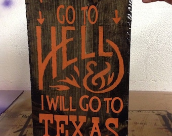 May include: A wooden sign with the text "You may all go to hell & I will go to Texas" in orange paint. The sign also features an outline of the state of Texas and the signature "Davy Crickett".