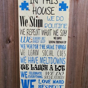 K&ouml;nnte beinhalten: Ein wei&szlig;es Holzschild mit blauen Puzzle-Teilen und schwarzem Text, der lautet: "In diesem Haus stimulieren wir, wir machen Routine, wir wiederholen, was wir sagen, wir haben eine sensorische Di&auml;t, wir schlafen selten, wir lieben es, Dinge auszurichten, wir sehen uns die gleichen Dinge an, wir lernen soziale Hinweise, wir haben Ausraster, wir lachen viel, wir feiern alles, wir machen soziale Geschichten, wir lieben hart, respektieren, akzeptieren."