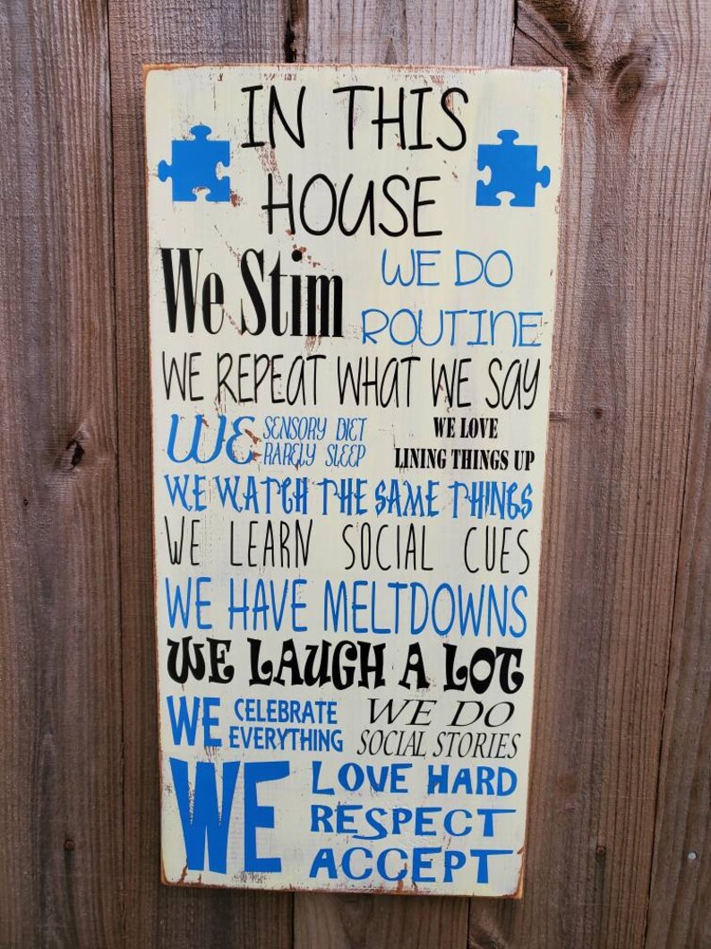 K&ouml;nnte beinhalten: Ein wei&szlig;es Holzschild mit blauen Puzzle-Teilen und schwarzem Text, der lautet: "In diesem Haus stimulieren wir, wir machen Routine, wir wiederholen, was wir sagen, wir haben eine sensorische Di&auml;t, wir schlafen selten, wir lieben es, Dinge auszurichten, wir sehen uns die gleichen Dinge an, wir lernen soziale Hinweise, wir haben Ausraster, wir lachen viel, wir feiern alles, wir machen soziale Geschichten, wir lieben hart, respektieren, akzeptieren."