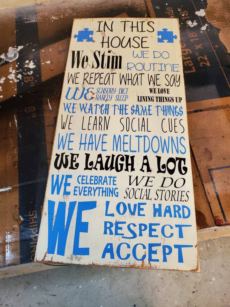 K&ouml;nnte beinhalten: Ein wei&szlig;es Holzschild mit blauem Text, der lautet: "In diesem Haus stimulieren wir, wir machen Routine, wir wiederholen, was wir sagen, wir... lieben stark, respektieren, akzeptieren". Das Schild hat zwei blaue Puzzle-Teile in den oberen Ecken.