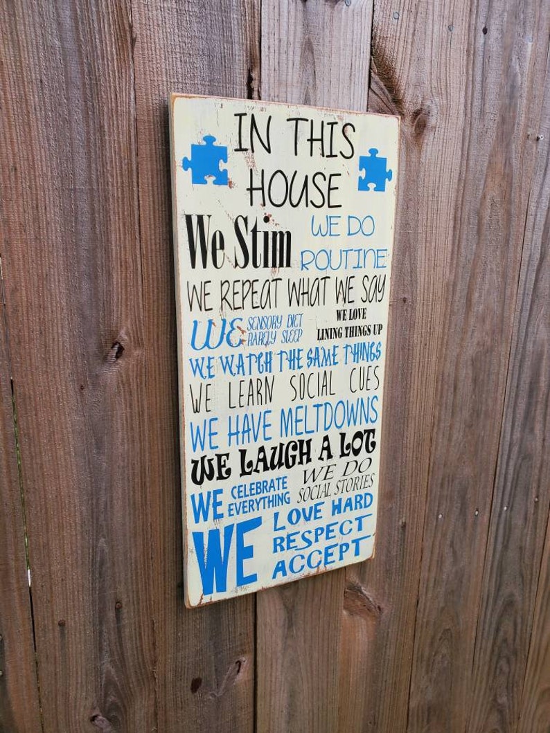 K&ouml;nnte beinhalten: Ein wei&szlig;es Holzschild mit blauem Text, auf dem steht: "In diesem Haus stimulieren wir, wir haben eine Routine, wir wiederholen, was wir sagen, wir machen eine sensorische Di&auml;t, wir lieben es, Dinge auszurichten, wir schauen uns die gleichen Dinge an, wir lernen soziale Hinweise, wir haben Ausbr&uuml;che, wir lachen viel, wir feiern alles, wir machen soziale Geschichten, wir lieben es sehr, wir respektieren, wir akzeptieren".
