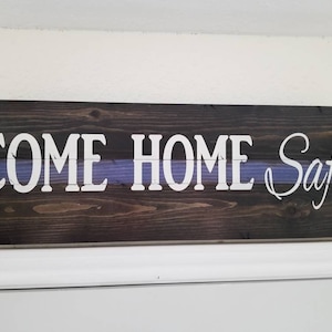 May include: Wooden sign with a dark brown stain and a thin blue stripe. The sign reads "Come Home Safe" in white lettering.