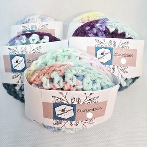 May include: Four colorful crocheted scrubbies with a white label that says "Uniquely Drawn Scrubbies".