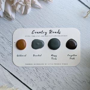 May include: A watercolor swatch card with four paint colors: Goldenrod, Riverbed, Messy Trails, and Forgotten Path. The card reads "Country Roads" and "Handmade Watercolors by Little Reverie Studio."