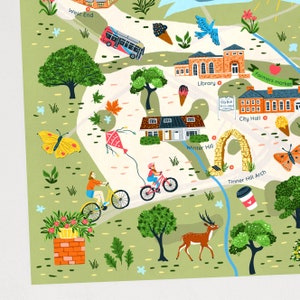 Op de afbeelding: Een grillige ge&iuml;llustreerde kaart van een stad met verschillende bezienswaardigheden, waaronder een bibliotheek, een stadhuis, een boerenmarkt en een Tinner Hill Arch. De kaart toont een bus, een hert, een vlinder, een vlieger en mensen die fietsen.