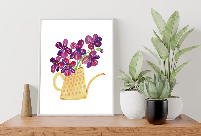 Puede incluir: Una regadera amarilla con estampado de lunares llena de flores moradas. La regadera tiene un pico y un asa. Las flores est&aacute;n dispuestas en un ramo.