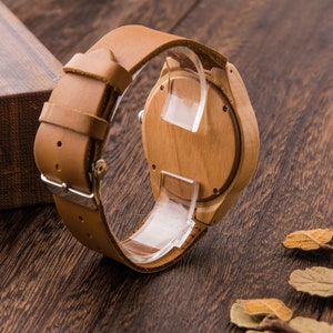 Puede incluir: Un reloj de pulsera de madera con una correa de cuero marr&oacute;n. La esfera del reloj es de madera y tiene un dise&ntilde;o sencillo.