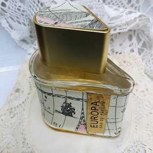 以下が含まれることがあります： 地図のデザインと「EUROPA EAU DE PARFUM」の文字が書かれた、金色と白の香水瓶です。