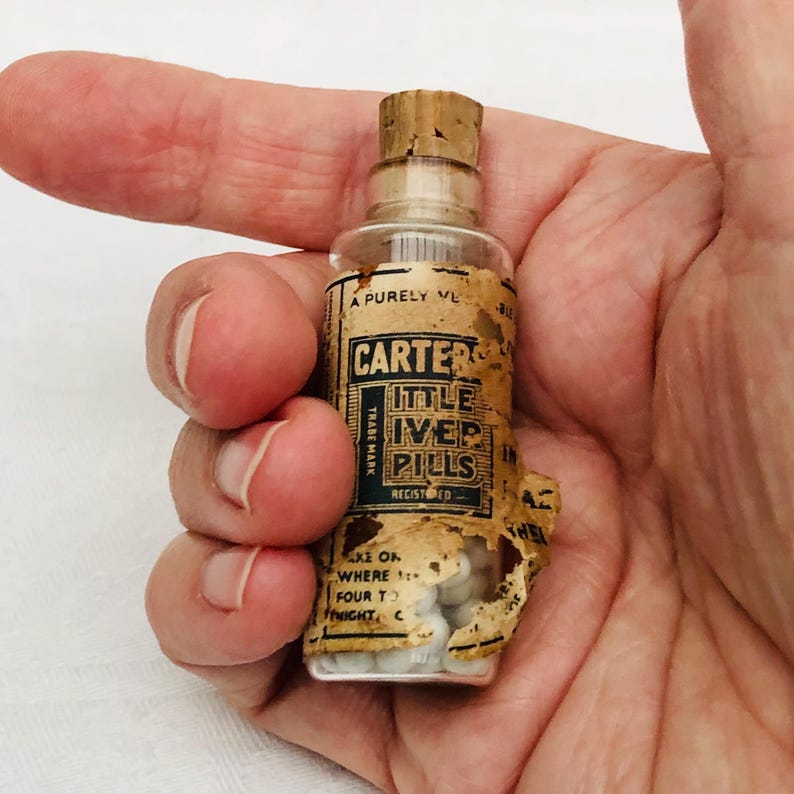 May include: A small glass bottle with a cork stopper filled with white pills. The label reads "Carter's Little Liver Pills" and "Trade Mark Registered".