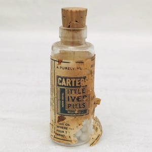 May include: A small glass bottle with a cork stopper and a label that reads "Carter's Little Liver Pills Registered Trade Mark". The bottle contains white pills.