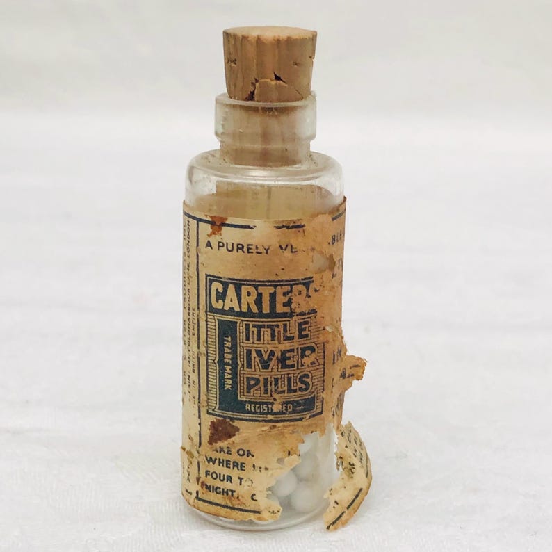 May include: A small glass bottle with a cork stopper and a label that reads "Carter's Little Liver Pills Registered Trade Mark". The bottle contains white pills.