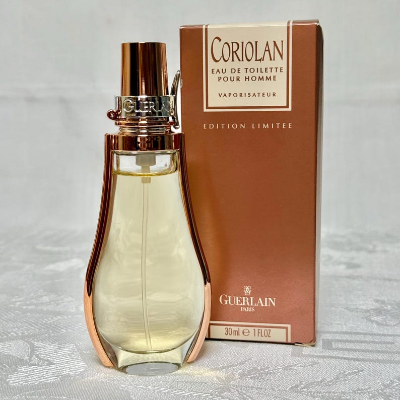 May include: A perfume bottle and box set. The bottle is a unique shape with gold accents and a clear glass body filled with a light yellow liquid. The box is a warm brown color with the text "CORIOLAN EAU DE TOILETTE POUR HOMME" and "EDITION LIMITEE". The bottle contains 1 fl oz.