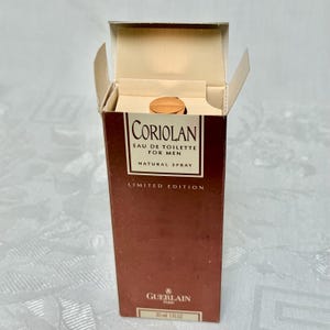 May include: An open box of Guerlain Coriolan Eau de Toilette for Men. The brown box has the product name and details in white text. The bottle is visible inside the box, with a gold-colored cap. The box is a limited edition.