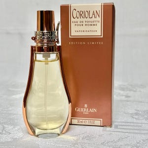 May include: A perfume bottle with a gold-colored cap and accents, next to a brown box. The bottle is filled with a light yellow liquid. The box reads "CORIOLAN EAU DE TOILETTE POUR HOMME VAPORISATEUR EDITION LIMITEE" and "30 ml e 1 FLOZ".