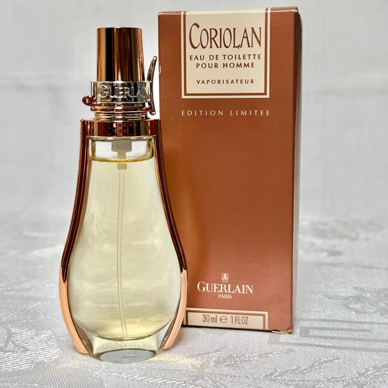 May include: A perfume bottle with a gold-colored cap and accents, next to a brown box. The bottle is filled with a light yellow liquid. The box reads "CORIOLAN EAU DE TOILETTE POUR HOMME VAPORISATEUR EDITION LIMITEE" and "30 ml e 1 FLOZ".