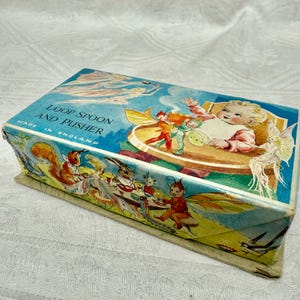 Puede incluir: Caja rectangular vintage con tapa azul con el texto "Loop Spoon and Pusher" e ilustraciones de hadas, un bebé y animales. Fabricado en Inglaterra.