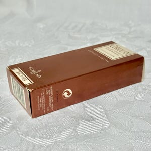May include: A brown rectangular box of Guerlain Coriolan Eau de Toilette Pour Homme. The box has the text "EDITION LIMITEE" and "30ml e 1 fl oz". The box is on a white patterned surface.